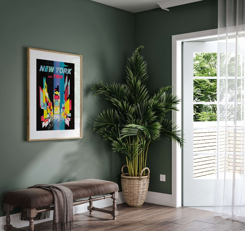 Pu&ograve; includere: Un poster incorniciato con un design grafico colorato dello skyline di New York City. Il poster &egrave; appeso a una parete verde salvia. Una palma in vaso si trova nell'angolo della stanza. Una panca di legno con una coperta &egrave; in primo piano.