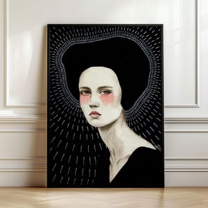 May include: A framed portrait print featuring a stylized figure with pale skin, dark hair, and prominent pink cheeks against a black background. The figure is surrounded by white radiating lines that create a halo effect within the rectangular frame.