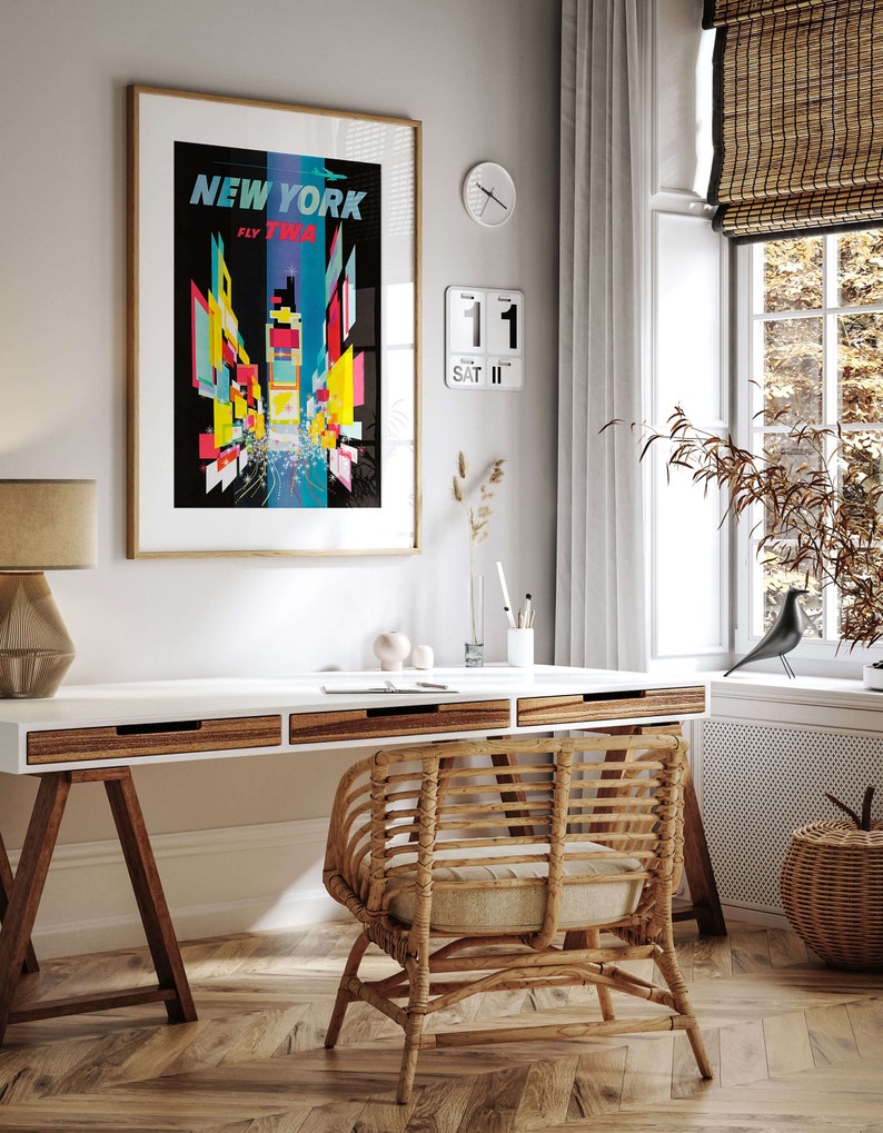 Pu&ograve; includere: Un ufficio domestico con una scrivania bianca, una sedia in vimini e un poster incorniciato che recita "NEW YORK FLY TWA". Il poster presenta un design colorato e astratto dello skyline di New York.