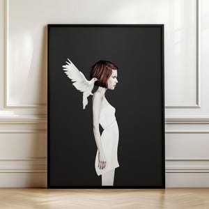 May include: A framed wall art print featuring a profile view of a person with short auburn hair wearing a simple white dress. A white dove with outstretched wings is perched on the person's shoulder against a solid dark charcoal background.