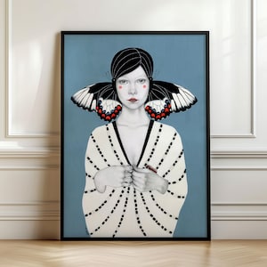 May include: A framed art print featuring a portrait of a person with dark hair and butterfly wings extending from the sides of their head. The person wears a white garment with black dotted vertical lines against a solid light blue background.