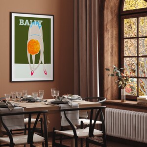 May include: A framed poster with the word "BALLY" in white text on a green background. The poster features a stylized illustration of a person in a blue swimsuit bending over with their head down. The person has orange hair and is wearing red shoes.