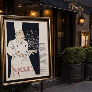 May include: A framed poster with a gold border stands outside a restaurant. The poster features an illustration of a chef in a white uniform, holding a sprig of flowers. The restaurant's name, "Maurice," is displayed in red script at the bottom of the poster.