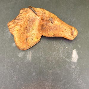 May include: A detailed, orange-brown horse head sculpture. The sculpture is a side profile, with visible details of the mane and facial features. The piece has a textured, aged appearance, suggesting it may be antique or vintage.