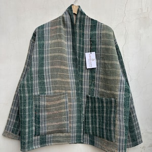 May include: A long-sleeved jacket featuring a green, white, and dark blue plaid pattern with a textured finish. The garment has an open front, two large square patch pockets, and a white rectangular tag labeled Laressa Gifts.