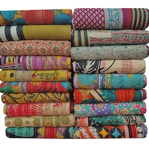 Op de afbeelding: Een stapel opgerolde, kleurrijke vintage kantha-quilts. De quilts tonen een verscheidenheid aan patronen en kleuren, waaronder bloemen-, geometrische en patchwork-ontwerpen. De tekst "Laressagifts" is zichtbaar op een van de quilts.