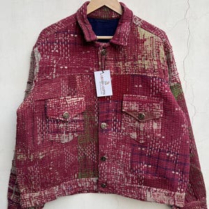 Könnte beinhalten: Eine langärmelige Jacke mit Patchwork-Design in den Farben Dunkelrot, Kastanienbraun und gedecktem Grün. Das Kleidungsstück hat einen Kragen, eine Knopfleiste, zwei Brusttaschen mit geknöpften Klappen und weiße Steppnähte. Ein Etikett zeigt LARESSA GIFTS.