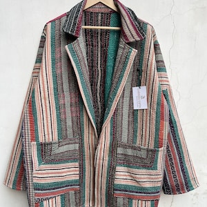 Op de afbeelding: Een jas met lange mouwen en een veelkleurig verticaal gestreept patroon in tinten teal, rood, zwart en crème. Het kledingstuk heeft een reverskraag, twee opgestikte zakken aan de voorzijde en een wit label met de tekst Laressa Gifts.