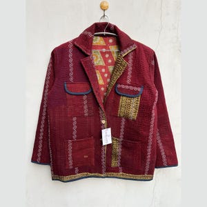 May include: A burgundy quilted jacket with a patterned interior and decorative stitching. The jacket has two front pockets, a notched collar, and a single button closure. The jacket is hanging on a metal hanger.