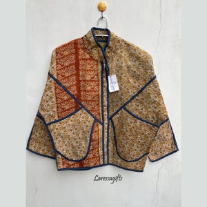 May include: A brown and orange quilted jacket with a blue trim and a zipper closure. The jacket has a mandarin collar and is made of a patchwork of different fabrics. The tag on the jacket reads "Laresagifts".