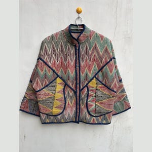 May include: A colorful quilted jacket with a geometric pattern in shades of red, green, yellow, and blue. The jacket has a stand-up collar and a zipper closure.