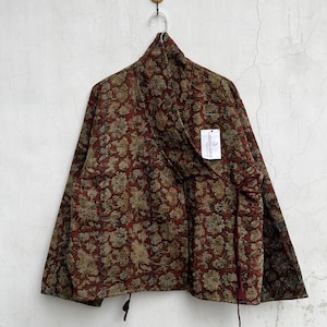 May include: A quilted wrap jacket in a deep rust-red color featuring an all-over floral pattern in muted gold and brown tones. The jacket has long sleeves, a wrap-front closure with thin fabric ties, and a white tag labeled LARESSA GIFTS.