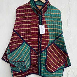 Puede incluir: Una chaqueta acolchada con un diseño de retazos en tela color granate y verde azulado con rayas horizontales doradas. La prenda tiene cuello alto, ribetes azul oscuro, dos bolsillos delanteros grandes y una etiqueta blanca LARESSA GIFTS.
