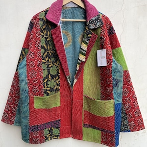Puede incluir: Una chaqueta de patchwork con una mezcla vibrante de paneles de tela en rojo, verde, azul y amarillo con costuras kantha. La chaqueta tiene cuello, mangas largas y dos bolsillos delanteros. Una etiqueta muestra el texto LARESSA GIFTS.