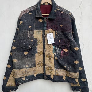 May include: A long-sleeve jacket featuring a patchwork design with dark charcoal, tan, and maroon fabric panels. The garment includes a collared neckline, button-front closure, two chest pockets with button flaps, and a tag labelled L.R.SS O'PTS.