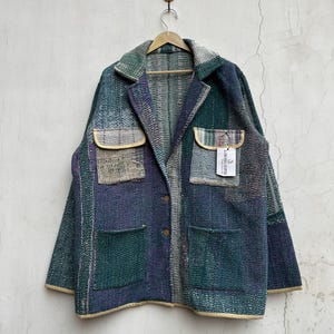 May include: A long-sleeve jacket crafted from multi-coloured patchwork fabric in shades of blue, green, and purple. The jacket features a notched collar, two chest pockets with flaps, two lower pockets, and two brown buttons. A tag reads LABESSA GIFTS.