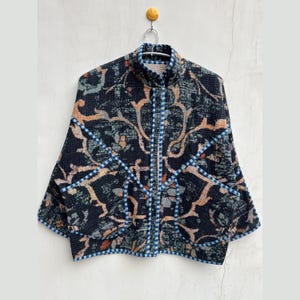 May include: A black and blue patterned jacket with a high collar and a zipper closure. The jacket has a unique design with a geometric pattern and a contrasting blue trim.