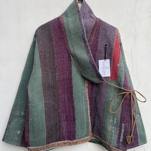 May include: A wrap-style jacket featuring vertical stripes in shades of purple, sage green, and dark brown. The garment has a wide collar, long sleeves, and a thin brown tie closure at the side. A white tag labeled LARESSA GIFTS is attached.