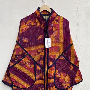 May include: A quilted jacket featuring a vibrant purple and orange leaf pattern with dark blue trim. The garment has a stand-up collar, long sleeves, and two large front pockets. A white tag labeled LARESSA GIFTS is attached to the front.