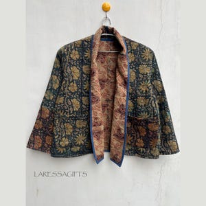 Könnte beinhalten: Wendejacke mit floralem Muster in Grün-, Gold- und Brauntönen. Die Jacke hat eine blaue Paspel und ein kontrastierendes Blumenmuster im Inneren. Der Text "LARESSAGIFTS" ist unten sichtbar.