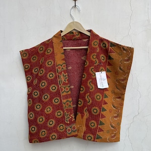 May include: A sleeveless vest made from quilted fabric featuring a deep red base with a repeating circular pattern. The front panels display contrasting mustard yellow borders with green triangular and floral motifs. A white tag reads LARESSA GIFTS.