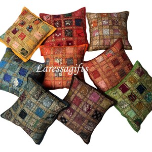 Op de afbeelding: Assortiment van acht kleurrijke vierkante kussens met ingewikkelde patchwork-ontwerpen en versieringen. De kussens zijn gemaakt van stof met verschillende texturen en patronen, waaronder pailletten, borduurwerk en kralen. De kussens zijn in een cirkelvormige opstelling op een witte achtergrond geplaatst.