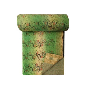 May include: A green and beige kantha quilt with a floral pattern. The quilt is rolled up and has a fringe on the edge.