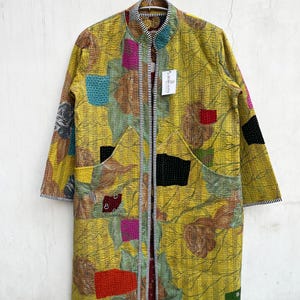 May include: A long-sleeved yellow jacket featuring a kantha-stitched floral pattern with multicolored fabric patches in red, black, and blue. The garment has a mandarin collar, two large front pockets, and black and white striped trim edges.