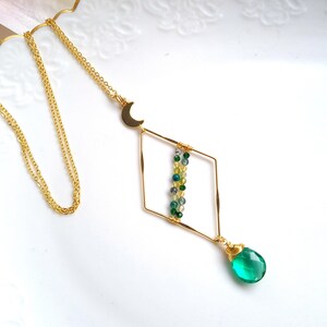 Könnte beinhalten: Eine goldene Halskette mit einem Halbmond-Anhänger und einem rautenförmigen Anhänger mit grünen und gelben Perlen. Der Anhänger hat einen grünen Edelstein-Tropfen.