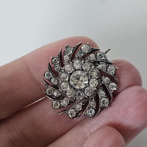 Op de afbeelding: Een zilveren broche met een draaiend ontwerp van heldere strass.