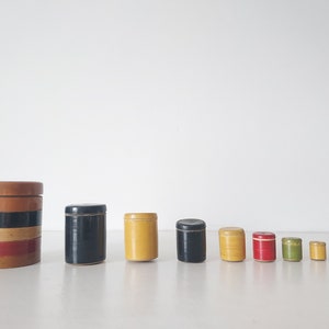 May include: A set of ten wooden nesting boxes in various sizes and colors, including brown, black, yellow, red, and green. The boxes are stacked in order of size, with the largest box on the left and the smallest box on the right.