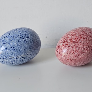 Puede incluir: Dos huevos de cerámica moteados, uno azul y otro rojo.