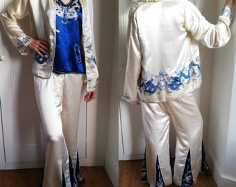 Puede incluir: Un conjunto de pijama de satén blanco con dragones bordados en azul. El conjunto incluye una chaqueta de manga larga y pantalones anchos.