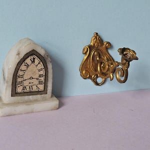 May include: A white marble clock with Roman numerals and a gold-tone wall sconce with a floral design.