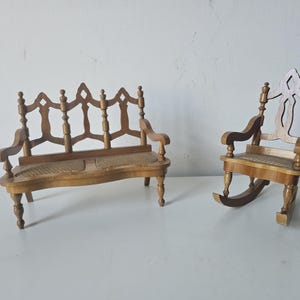May include: A miniature wooden bench and rocking chair set. The bench has a woven seat and ornate back. The rocking chair also has a woven seat and a decorative back. Both pieces are made of light-colored wood.
