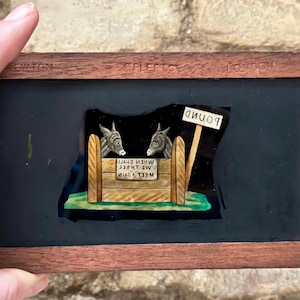 May include: A vintage glass slide depicting two donkeys in a wooden pen with a sign that reads "Pound". The text on the slide reads "Meet Again When Three We Shall See".