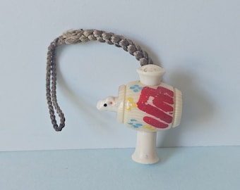 May include: A white plastic toy with a red, yellow, and blue painted design. The toy is shaped like a barrel with a small animal head on one side. It has a string attached to the top.