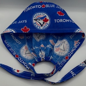 May include: A blue Toronto Blue Jays baseball cap with a repeating pattern of the team logo and text. The cap has a tie closure and is made of fabric. The team logo includes a blue jay bird and a red maple leaf.
