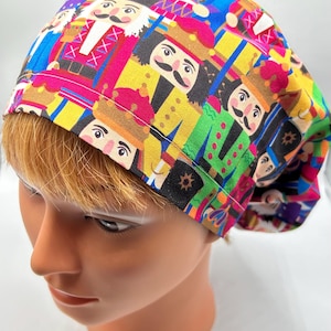 Könnte beinhalten: Eine bunte OP-Mütze mit einem sich wiederholenden Muster von Nussknackerfiguren. Die Mütze ist aus einem weichen, atmungsaktiven Stoff gefertigt und bietet eine bequeme Passform.