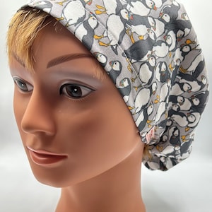 May include: A fabric scrub cap with a repeating pattern of puffins in shades of grey, white, and yellow. The cap is designed to cover the head. The puffins are depicted in various poses. The cap is a practical item.