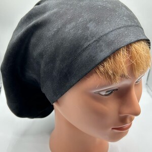 May include: A black scrub cap made from a soft, stretchy fabric. The cap has a simple design with a single seam around the edge.