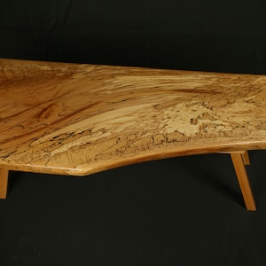 Könnte beinhalten: Ein rustikaler Holz-Couchtisch mit einer Live-Edge-Oberfläche und einer natürlichen Holz-Oberfläche. Der Tisch hat eine einzigartige, unregelmäßige Form und wird von vier einfachen Beinen getragen.