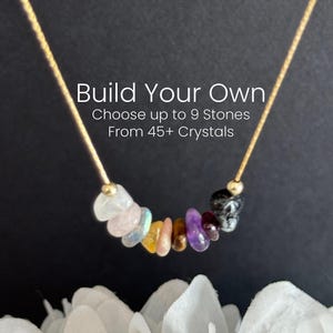 May include: A gold chain necklace with a variety of colorful gemstones. The necklace features a selection of stones in shades of white, pink, yellow, orange, purple, and black. Text on the image reads "Build Your Own" and "Choose up to 9 Stones From 45+ Crystals."