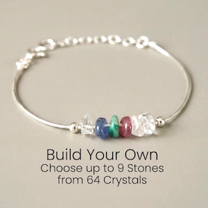 May include: A silver bracelet with a series of colorful gemstones. The bracelet features clear, blue, green, red, and white stones. Text on the image reads "Build Your Own" and "Choose up to 9 Stones from 64 Crystals."