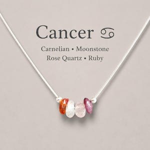 May include: A silver-toned chain necklace featuring four small, irregular tumbled gemstone beads in shades of orange, white, pale pink, and deep red. The text Cancer, the crab symbol, and the words Carnelian, Moonstone, Rose Quartz, and Ruby appear.