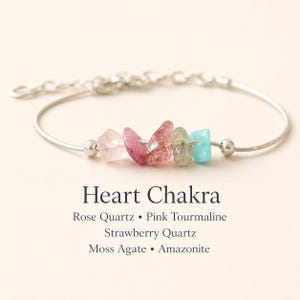 May include: A silver bracelet with five gemstone beads in shades of pink, green, and blue. The bracelet includes rose quartz, pink tourmaline, strawberry quartz, moss agate, and amazonite. Text reads "Heart Chakra".
