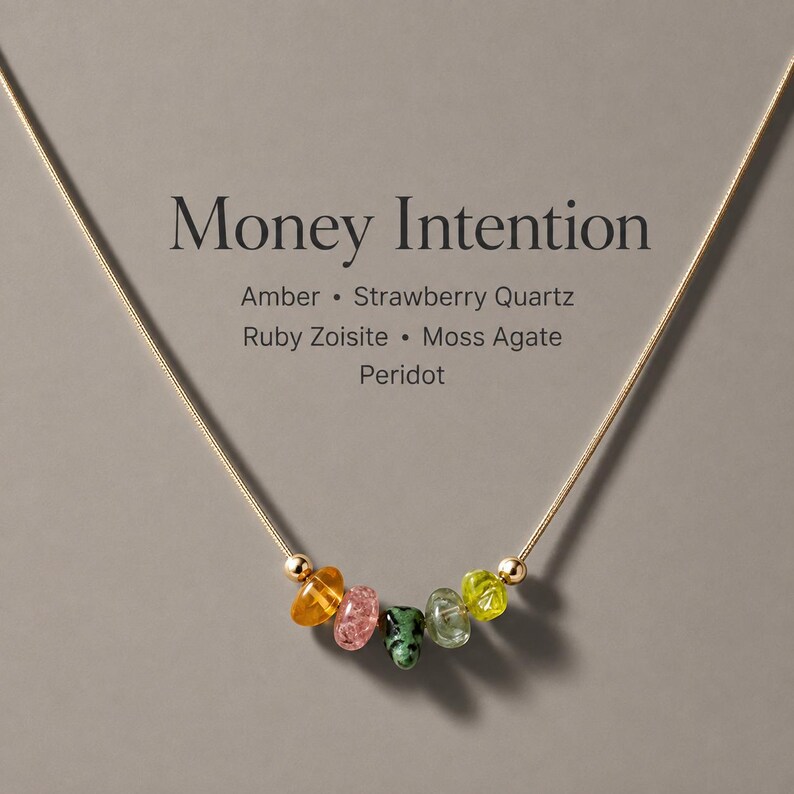May include: A gold-tone chain necklace featuring five small, irregular tumbled gemstones in amber, pink, green, and yellow, flanked by two gold-tone beads. The text reads: Money Intention, Amber, Strawberry Quartz, Ruby Zoisite, Moss Agate, Peridot.