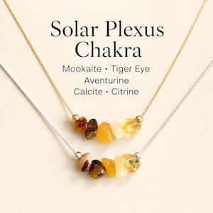 Può includere: Due collane con pietre del chakra del plesso solare. La collana superiore ha una catena d'oro e la collana inferiore ha una catena d'argento. Le collane presentano pietre di Mookaite, Occhio di Tigre, Avventurina, Calcite e Citrino. Il testo "Solar Plexus Chakra" è in alto.