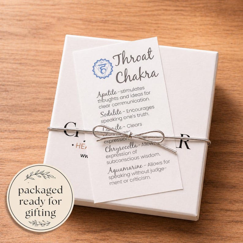 May include: A white gift box tied with silver string, featuring a card labeled "Throat Chakra." The card lists properties of gemstones like Apatite and Aquamarine. A round sticker reads "packaged ready for gifting."
