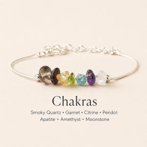 May include: A silver bracelet featuring seven colorful gemstone beads: smoky quartz, garnet, citrine, peridot, apatite, amethyst, and moonstone. The word "Chakras" is displayed below the bracelet.